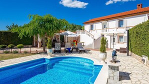 A swimming pool with lounge chairs, a stone pathway, and a white building with a red roof.