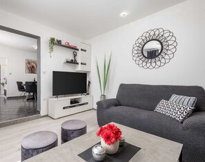 A modern living room with a flat-screen TV, grey sofa, ottomans, and a decorative mirror.