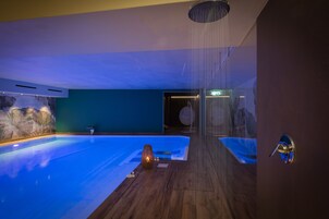 Una piscina interior moderna con suelo de madera, pared de piedra y puerta de cristal que da a otra habitación.