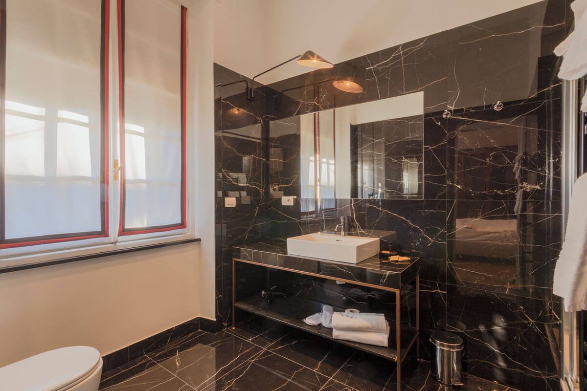 A modern bathroom with a large mirror, black marble walls, and a white sink.