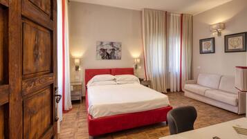Een hotelkamer met een groot bed, een rood hoofdeinde, een witte bank, een houten vloer en een bureau met een afstandsbediening.
