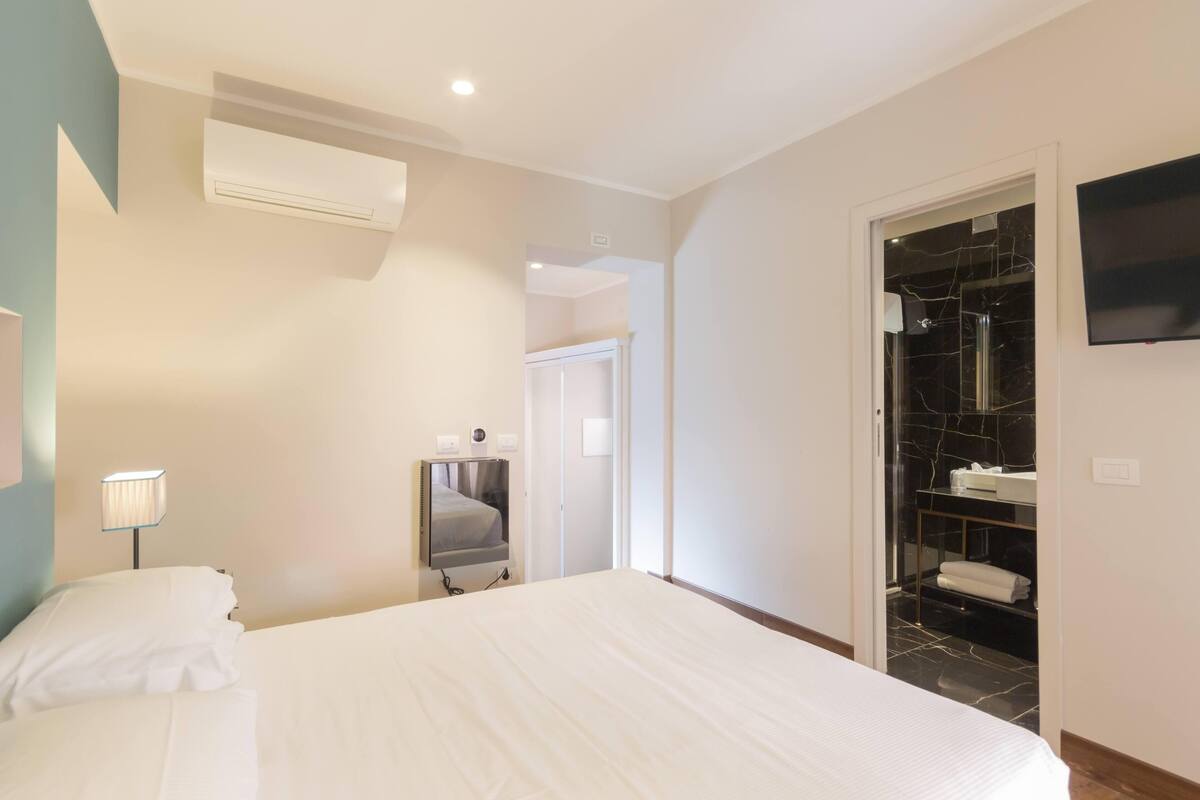 Hotelkamer met een bed, een televisie, een spiegel, een kledingkast en een badkamer zichtbaar door een geopende deur.