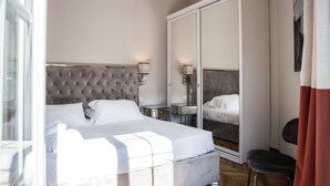Ein modernes Hotelzimmer mit einem großen Bett, einem Kleiderschrank, einem Schminktisch mit Spiegel und einem kleinen Tisch.