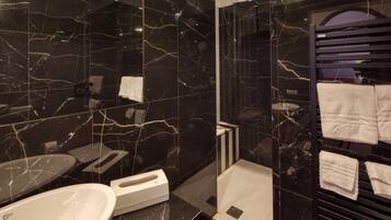 Une salle de bain moderne avec des murs en marbre noir, un lavabo blanc et un porte-serviettes avec plusieurs serviettes.