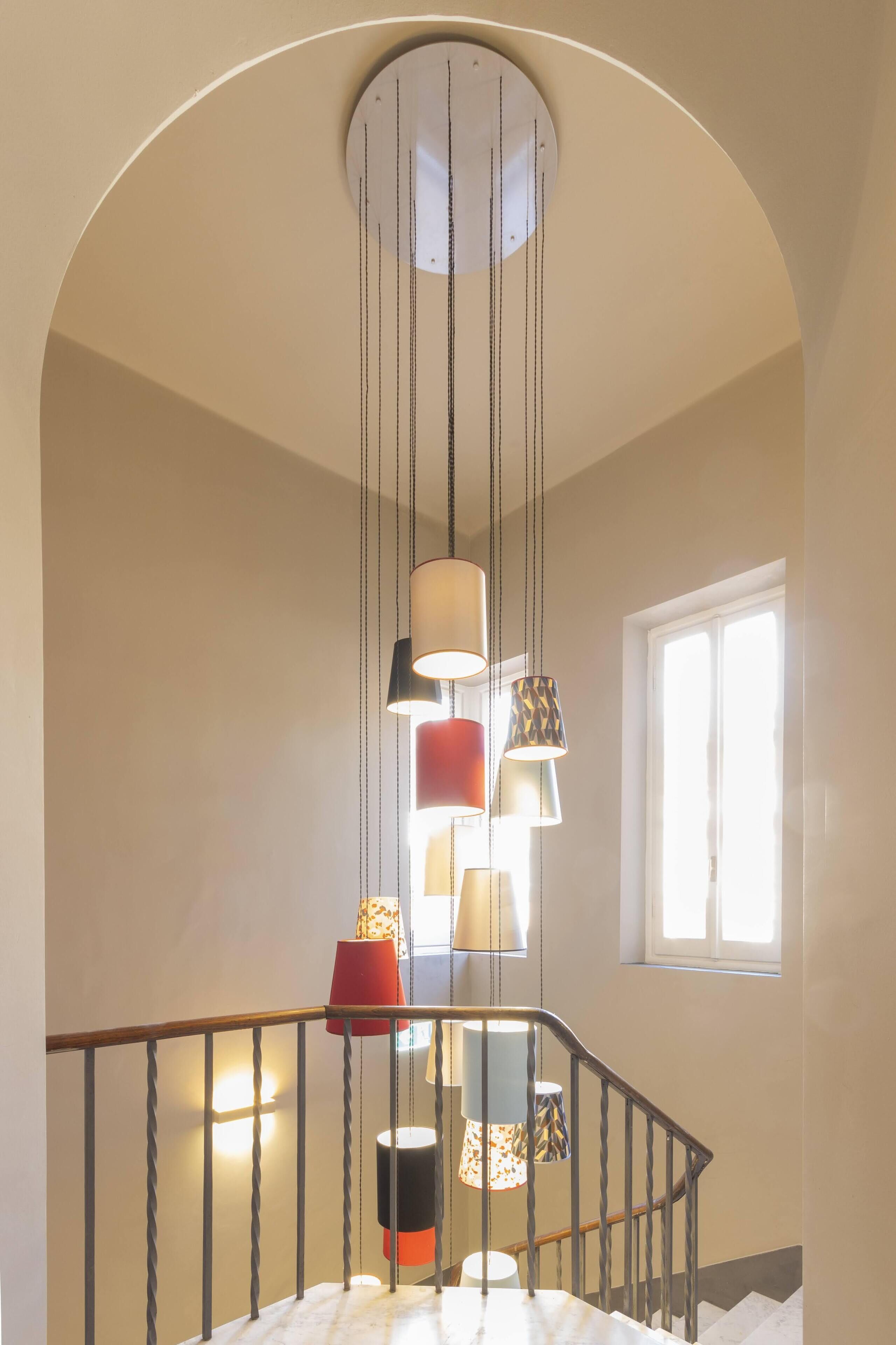 Una escalera con techo curvo, barandal de madera y lámparas colgantes con pantallas decoradas.