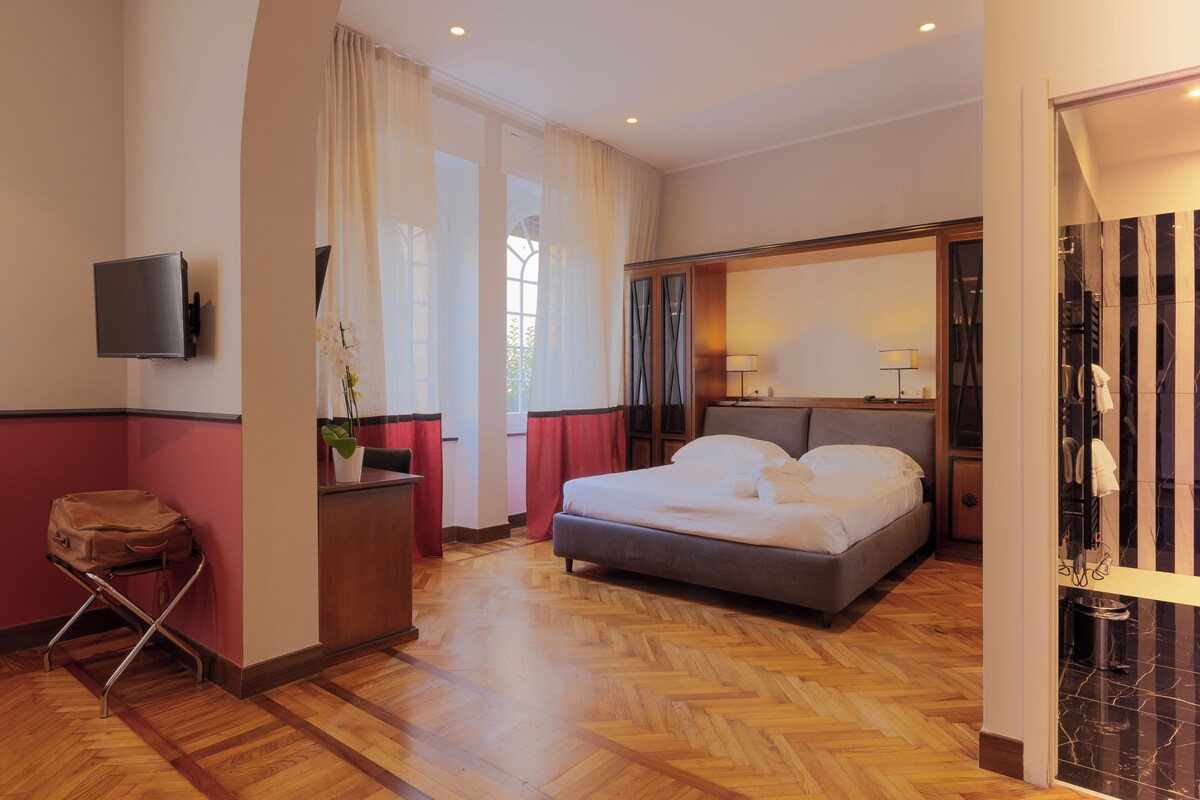 Habitación de hotel con cama, escritorio, silla, televisión y baño privado con ducha e inodoro.
