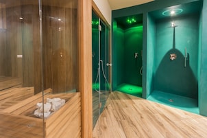 A modern bathroom with a wooden floor, a glass-enclosed shower, and a green-tinted wall.