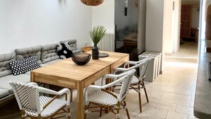 Ett modernt kök med ett matbord i trä, stolar i rotting, en grå soffa och en hängande lampa.