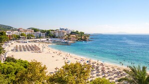 En strand vid kusten med ett hotellkomplex, inklusive parasoller och solstolar.