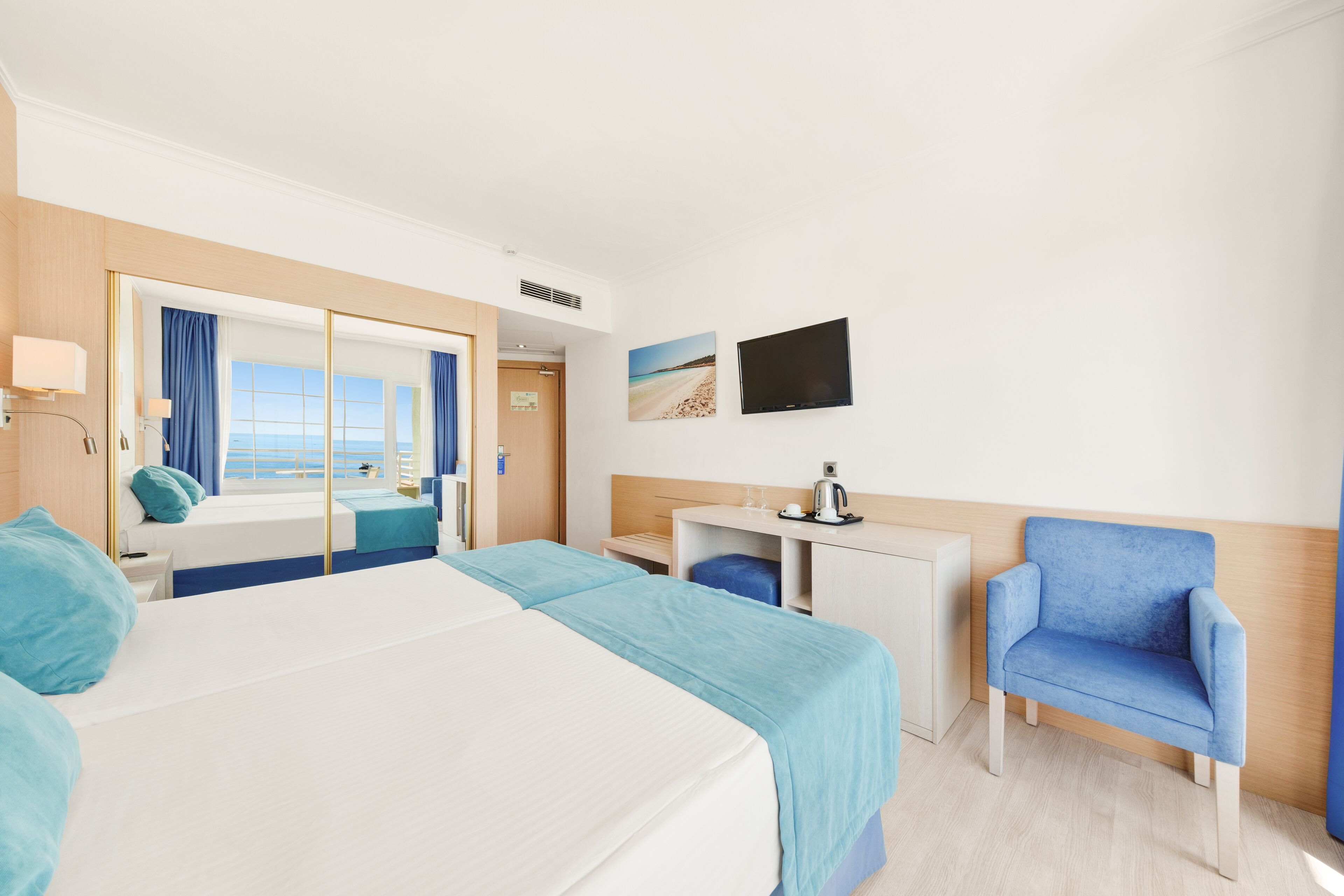 A hotel room with a large bed, a desk, a chair, and a TV on the wall.