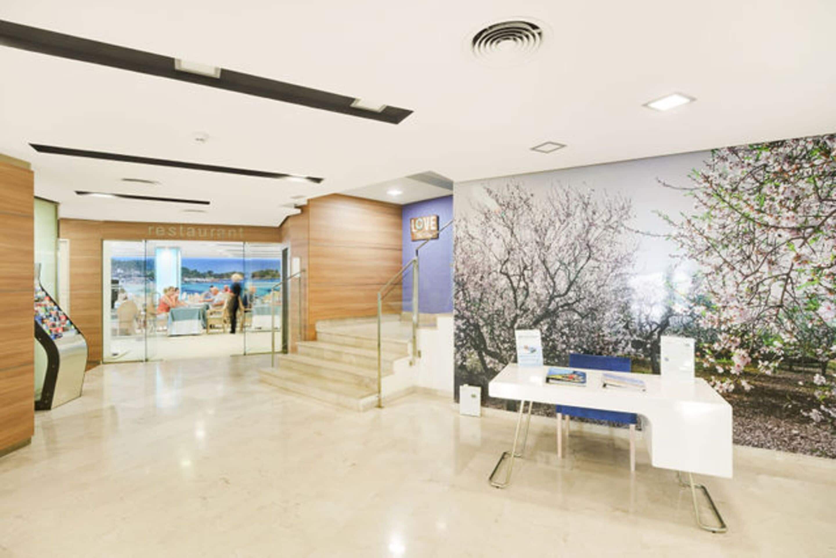 Un interior moderno con una recepción, una escalera y un mural de árboles.