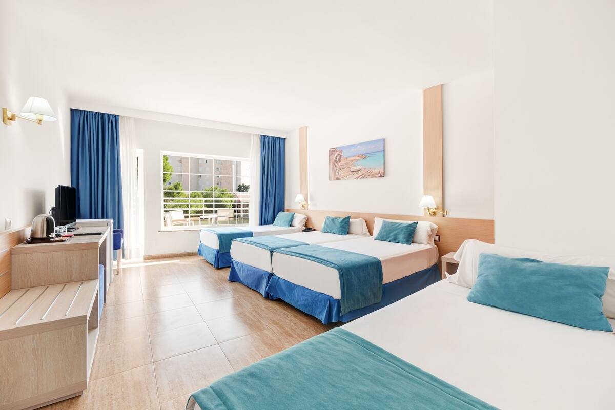 Quarto de hotel com duas camas, uma mesa, uma cadeira, televisão e janela com cortinas.