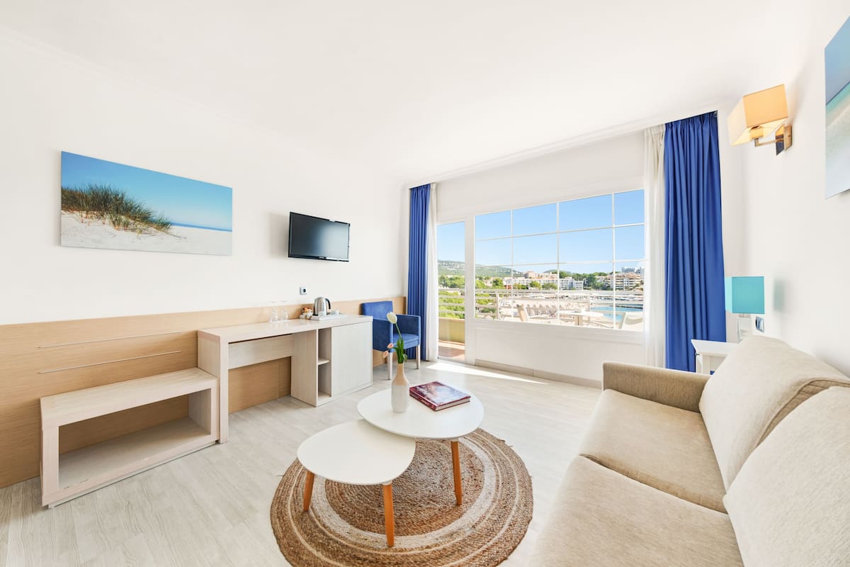 Quarto de hotel moderno com uma grande janela, televisão de tela plana, sofá, mesa pequena e escrivaninha.