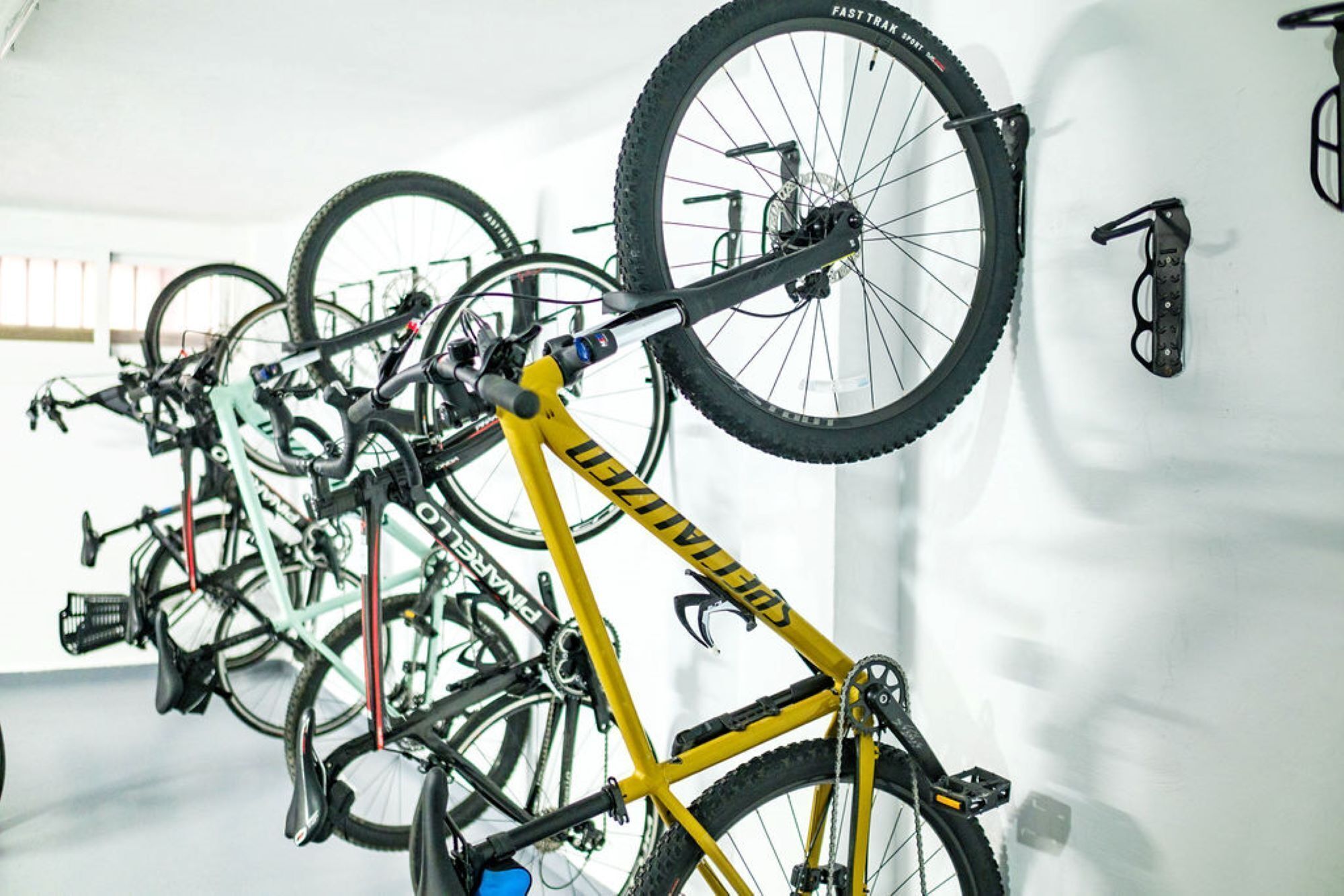 Un aparcaciclos con varias bicicletas, incluyendo una amarilla, en una habitación con paredes blancas y una puerta con manija.