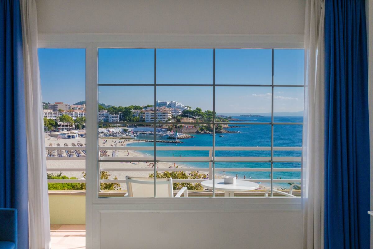Quarto com uma grande janela com vista para a praia e para a paisagem urbana.