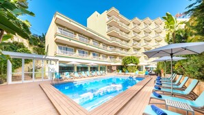 Ett hotell med en swimmingpool, solstolar och en stor byggnad med flera balkonger.