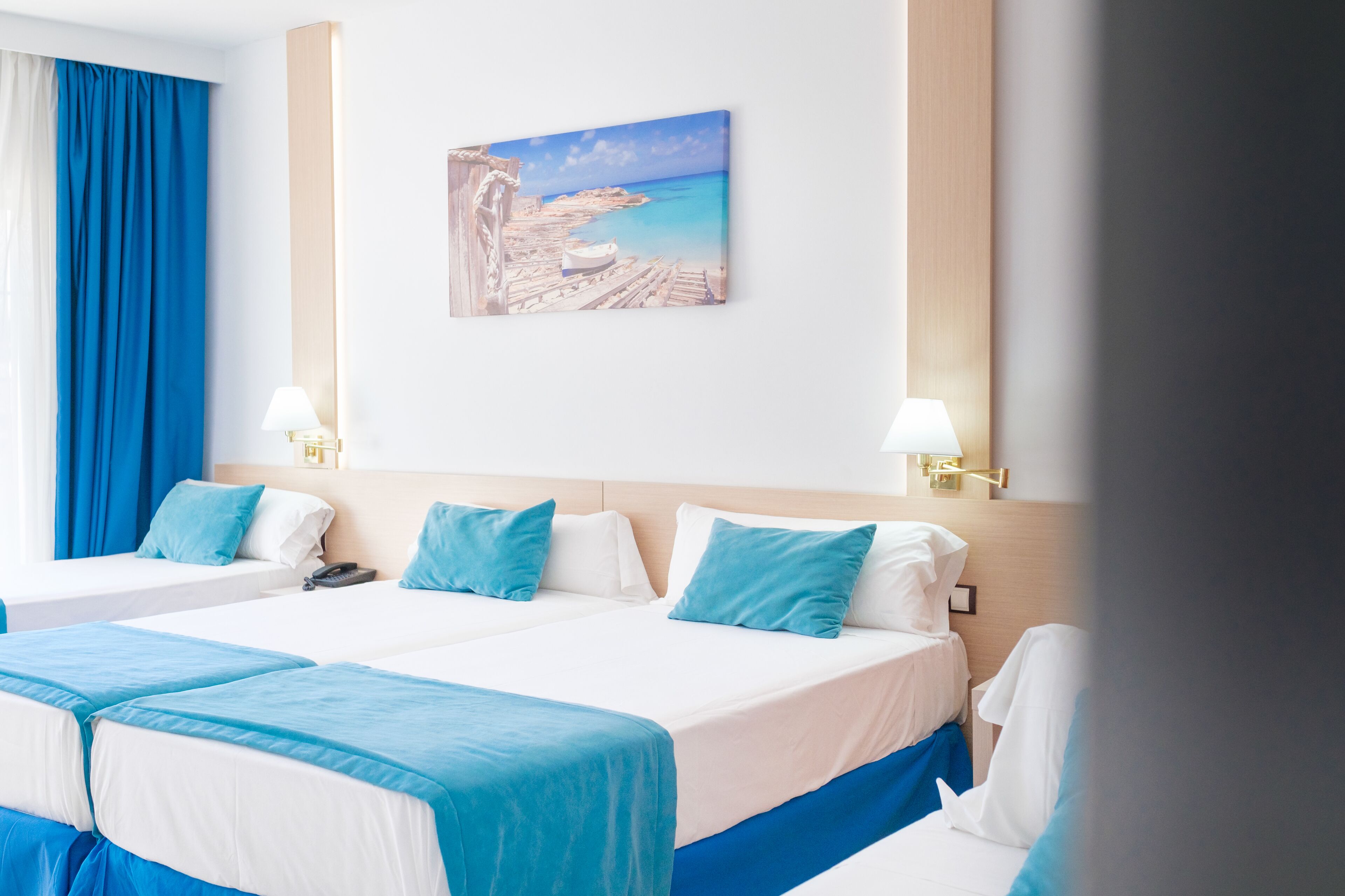 Een hotelkamer met twee bedden, een schilderij van een strandlandschap en uitzicht op zee.