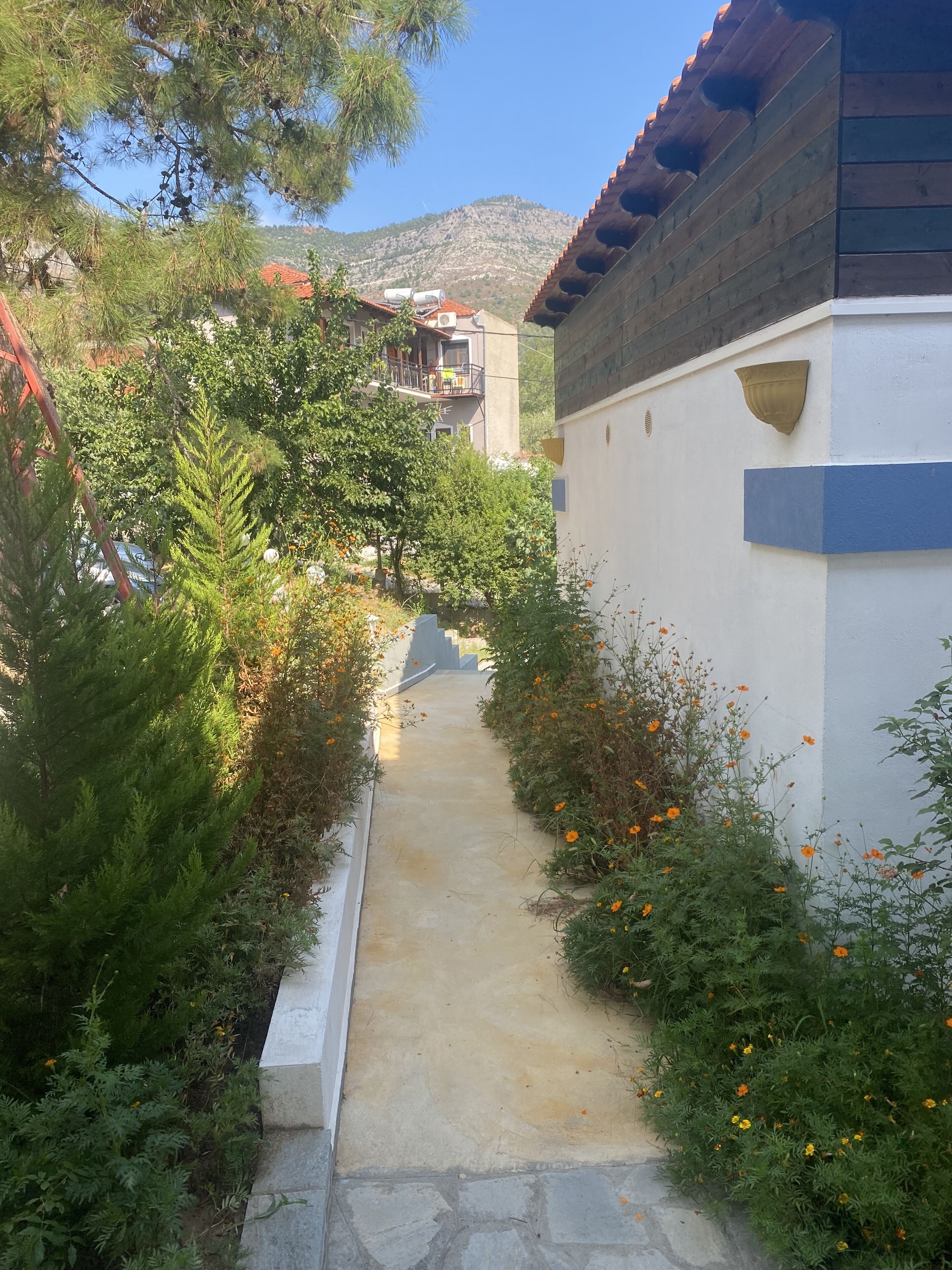 Un étroit sentier bordé de verdure et un bâtiment doté d’un toit en tuiles.