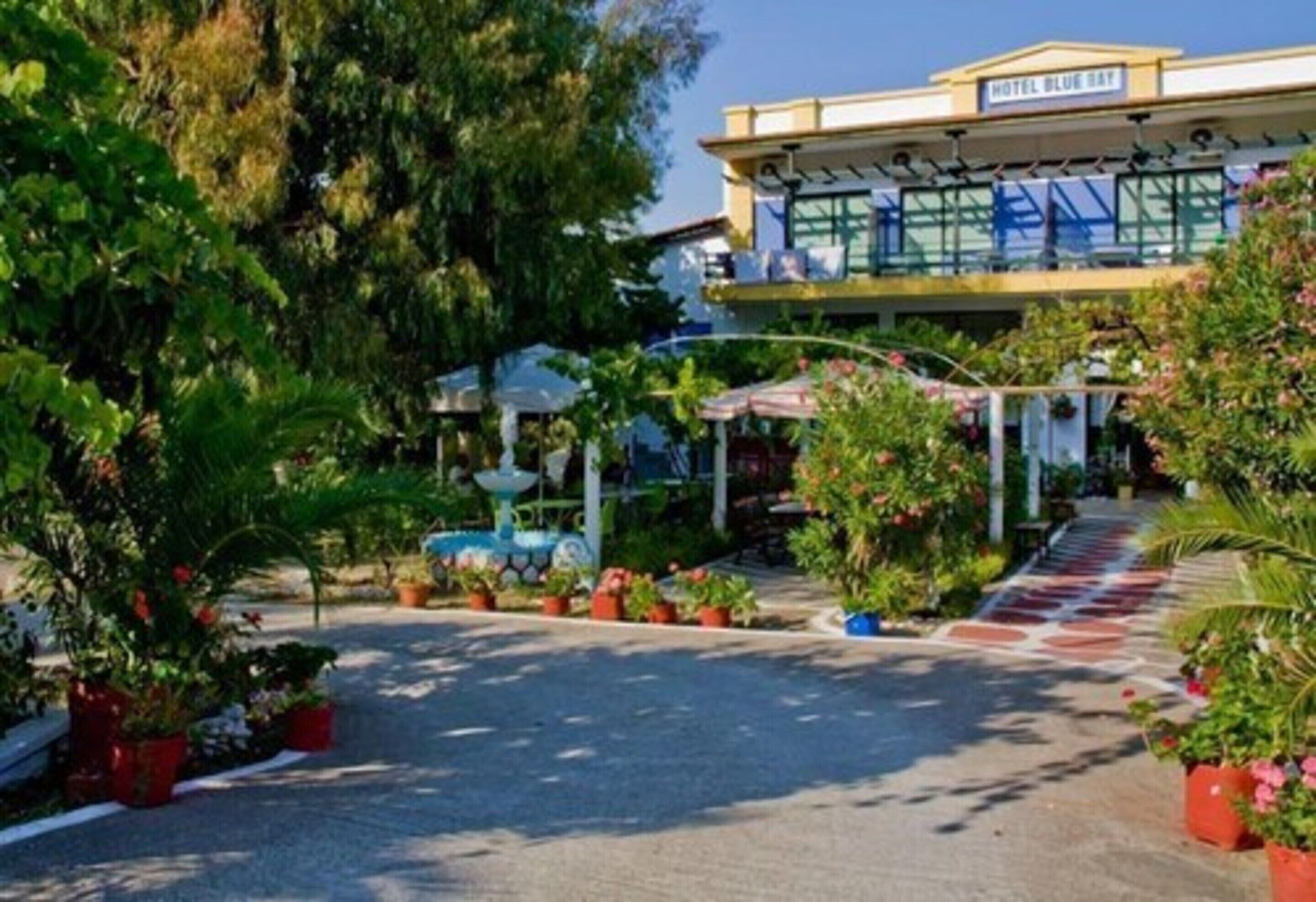 Entrada de hotel con galería techada, plantas en macetas y cielo despejado.