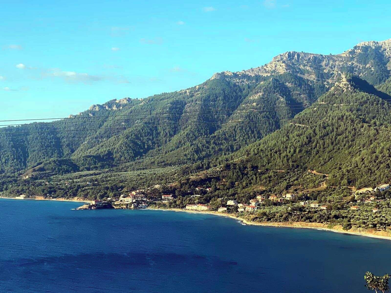 A coastal town with a mountainous backdrop, featuring a mix of residential buildings and natural landscapes.