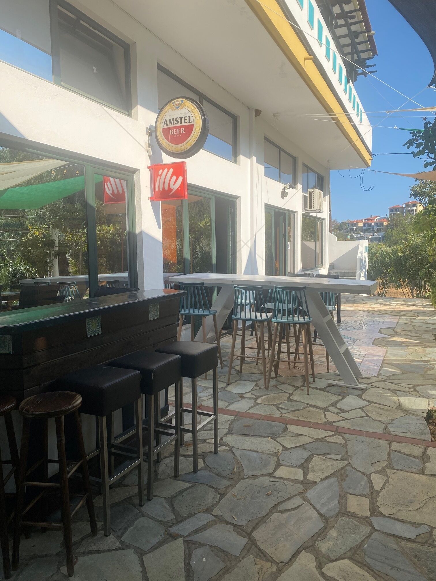 An outdoor seating area with stone flooring, a bar with stools, and a sign for Amstel Beer.