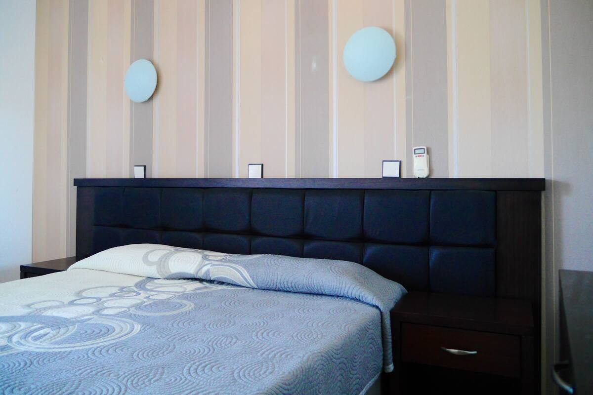A hotel room with a dark headboard, a bed with a patterned bedspread, and a striped wall with two circular wall decorations.