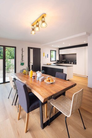 A modern kitchen with a central island, a dining area with a wooden table, and a view of the outdoors. - Villa Odet O Bord de l'O Piscina coberta 29°C em Sainte Marine, praia 100m (Combrit)