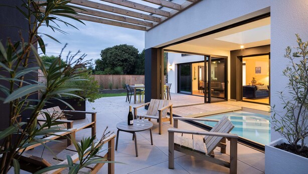 An outdoor patio with wooden furniture, a glass table, and a pool. - Villa Odet O Bord de l'O Piscina coberta 29°C em Sainte Marine, praia 100m (Combrit)