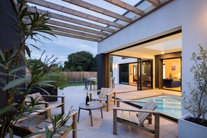 An outdoor patio with wooden furniture, a glass table, and a pool. - Villa Odet O Bord de l'O Piscina coberta 29°C em Sainte Marine, praia 100m (Combrit)