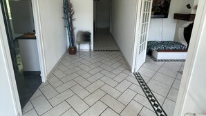 Un couloir avec des carreaux disposés en motif chevrons, un luminaire suspendu et une porte donnant sur une pièce où se trouvent un lit et un téléviseur.