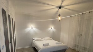 Une chambre à coucher avec un lit, deux lampes fixées au mur, un luminaire suspendu et un rideau.