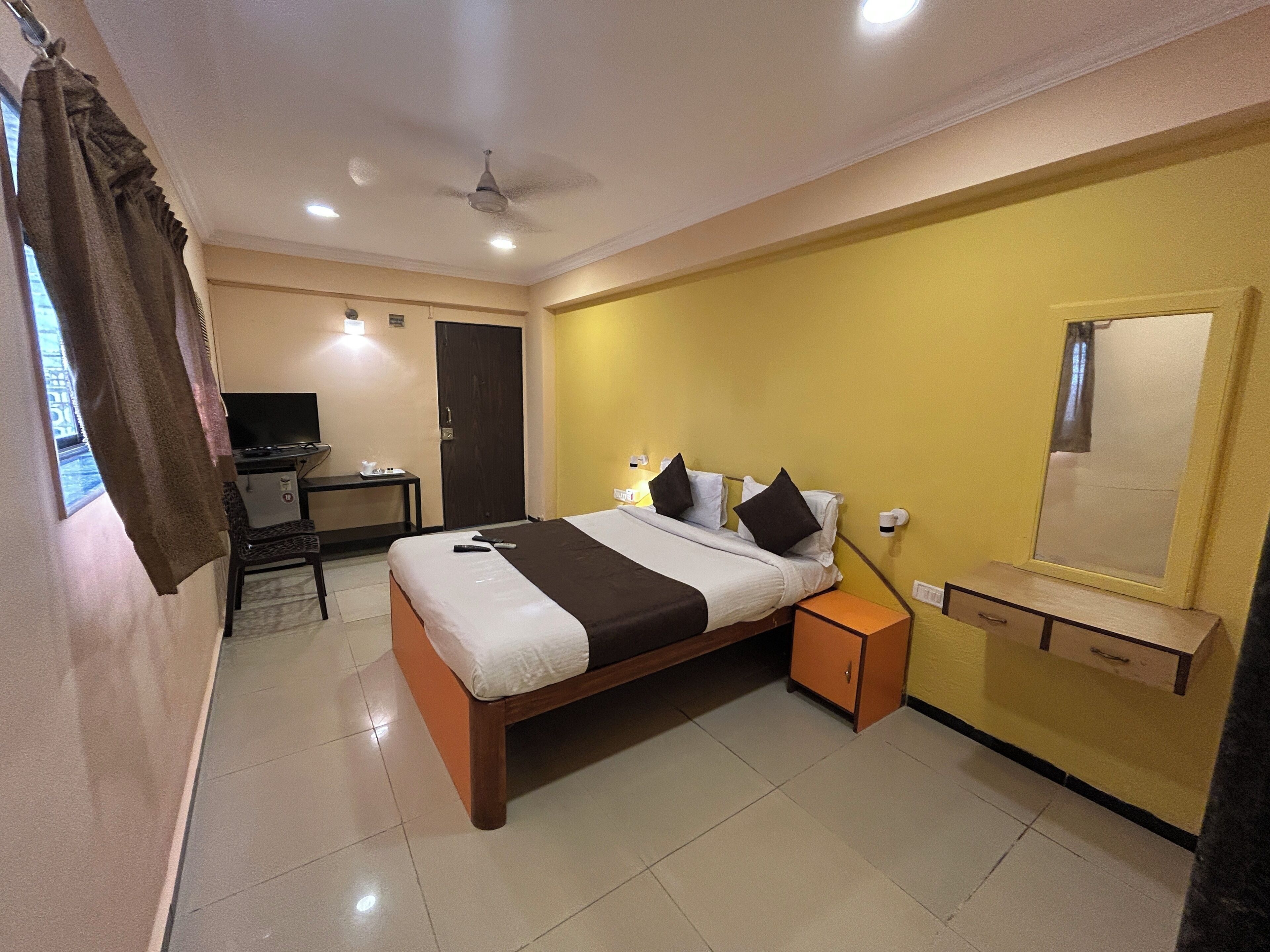 A hotel room with a bed, bedside table, a desk with a chair, a television, and a door.