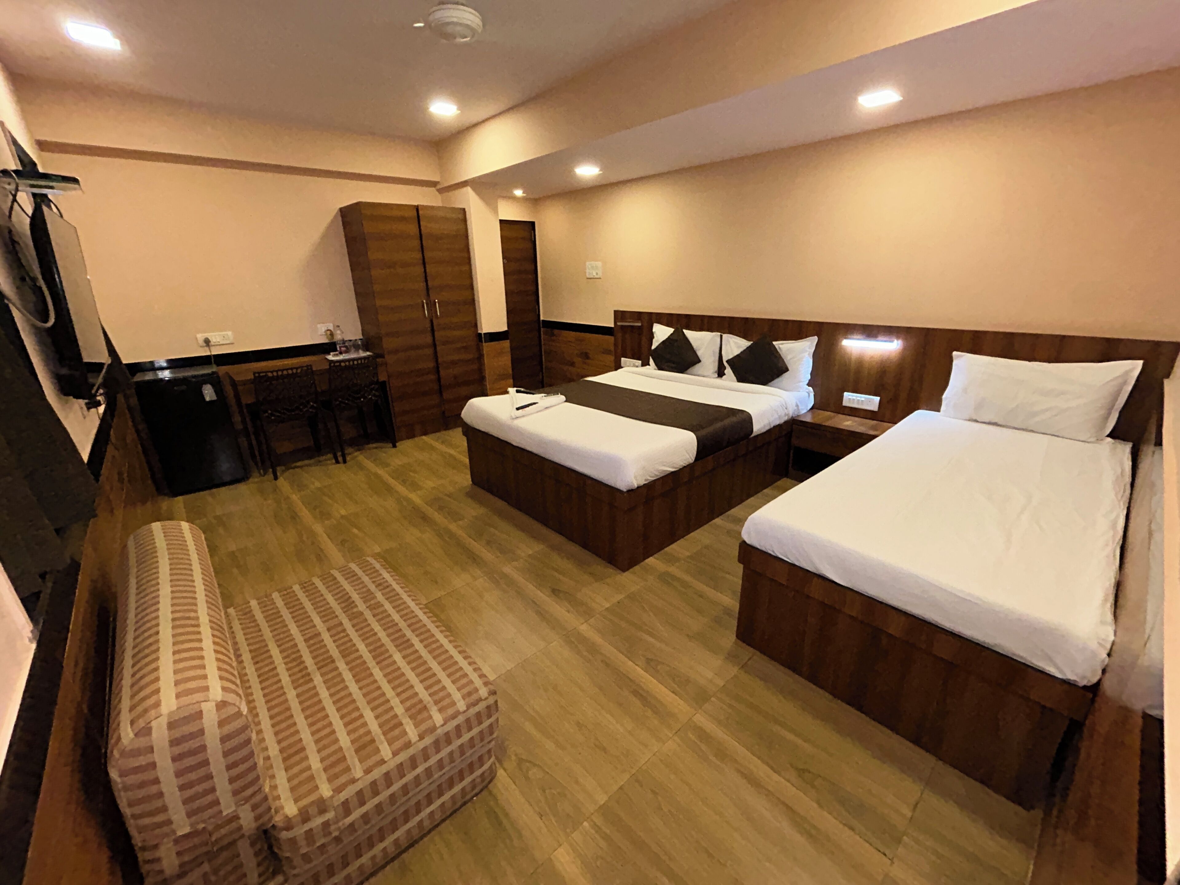 A hotel room with two beds, a desk, a wardrobe, and a bench.