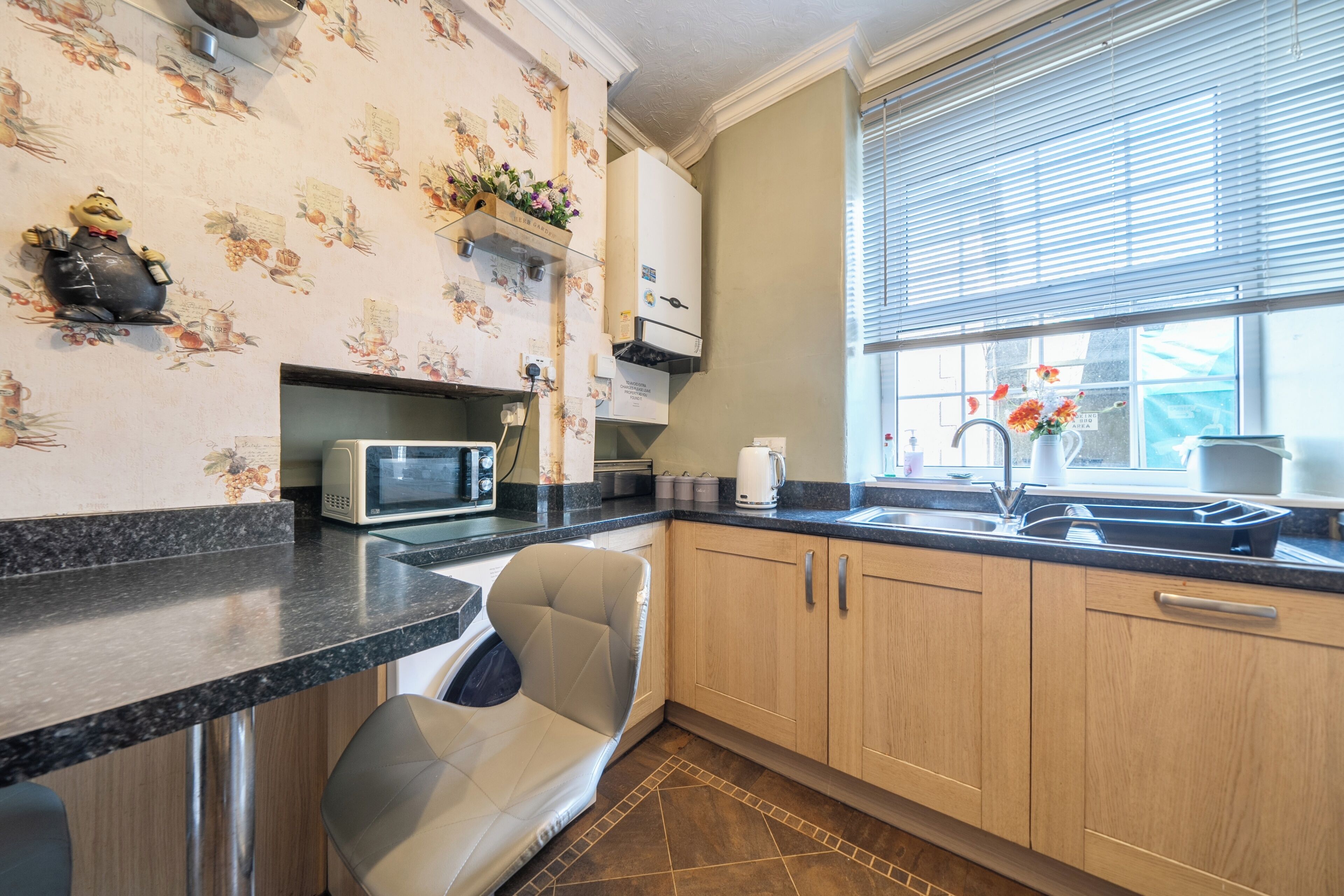 A kitchen with a microwave, sink, and a chair.