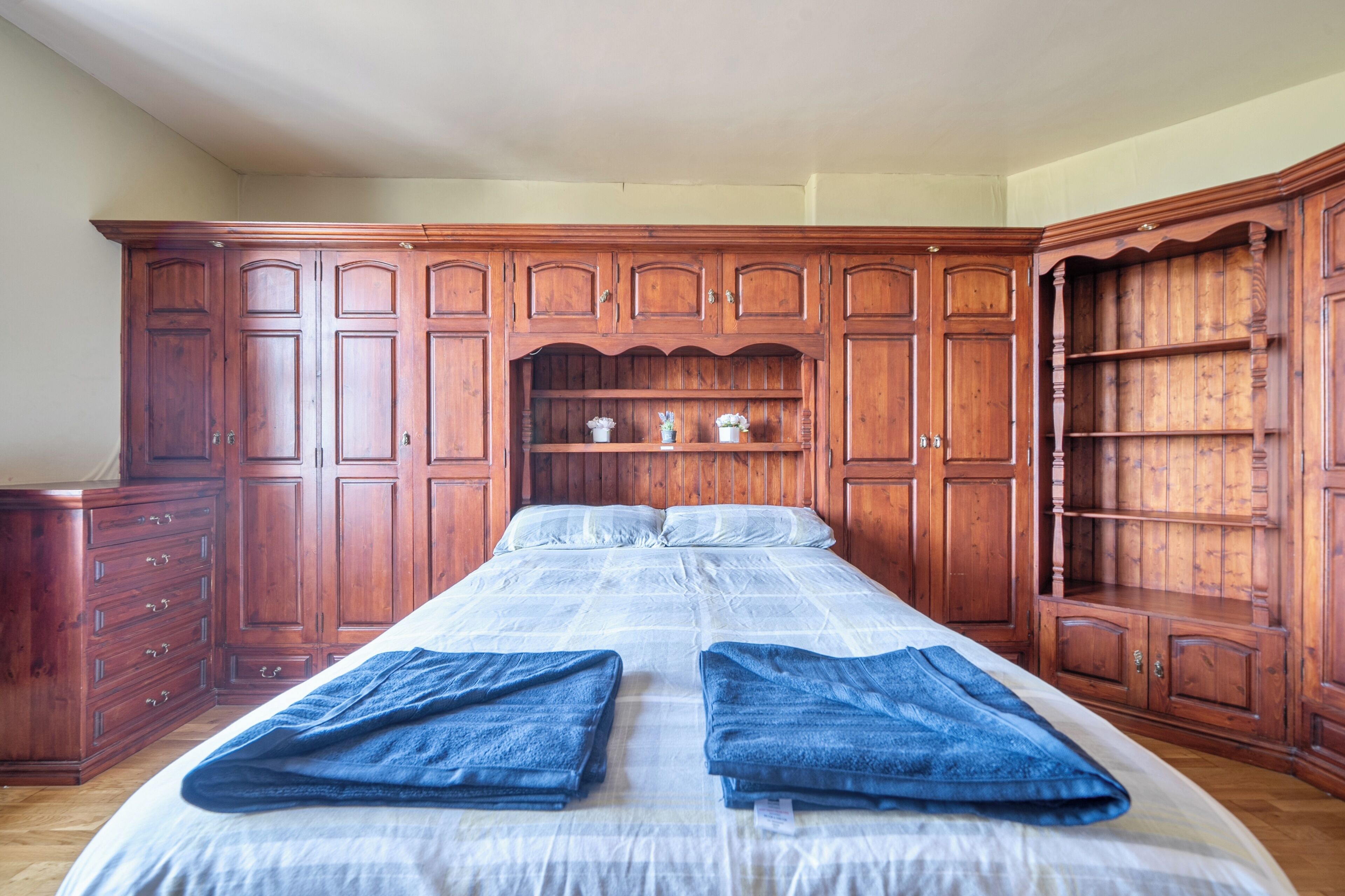 A bedroom with a large bed, wooden wardrobe, and a dresser.