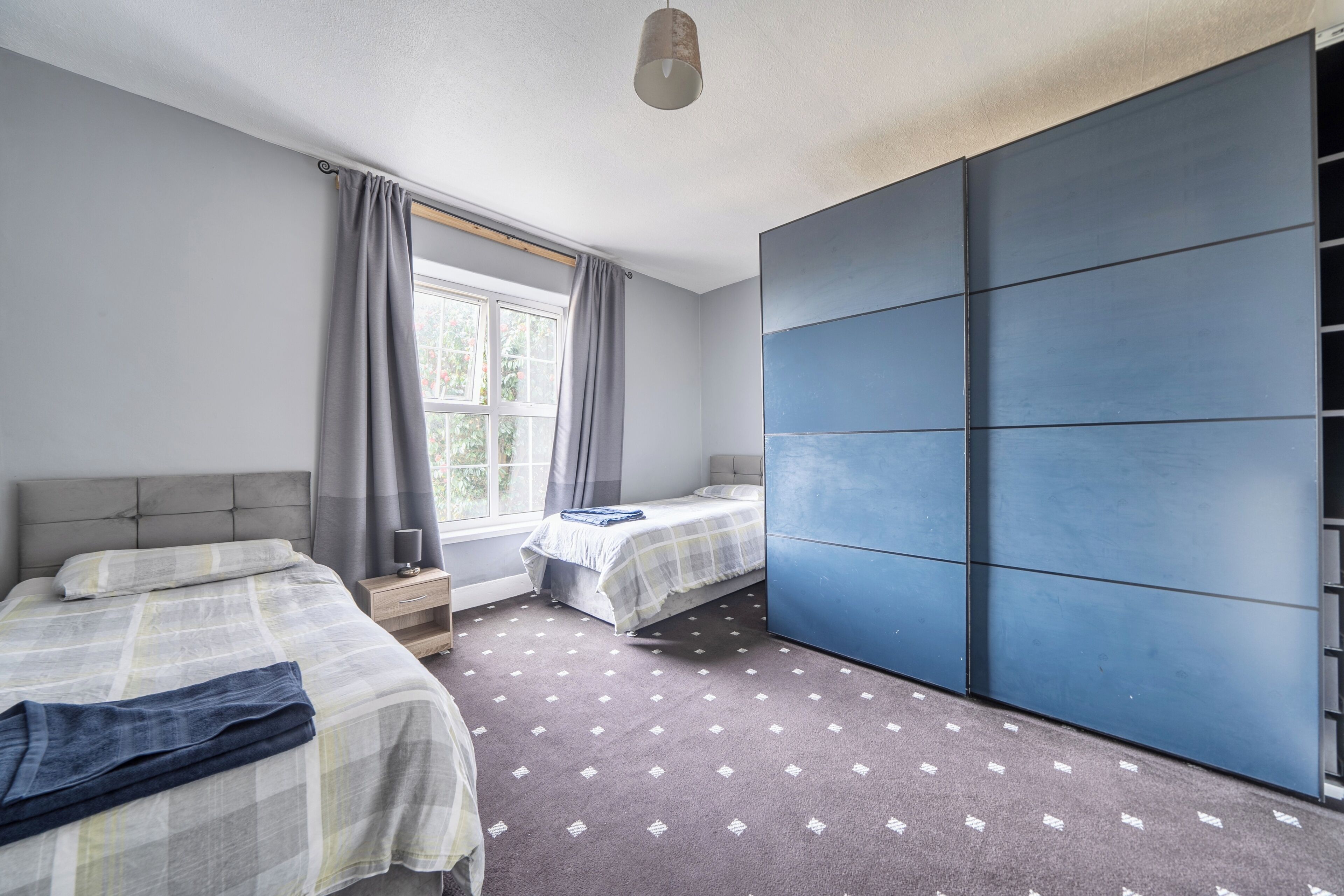 Une chambre avec deux lits, une grande armoire, une fenêtre avec des rideaux et un tapis à motifs.