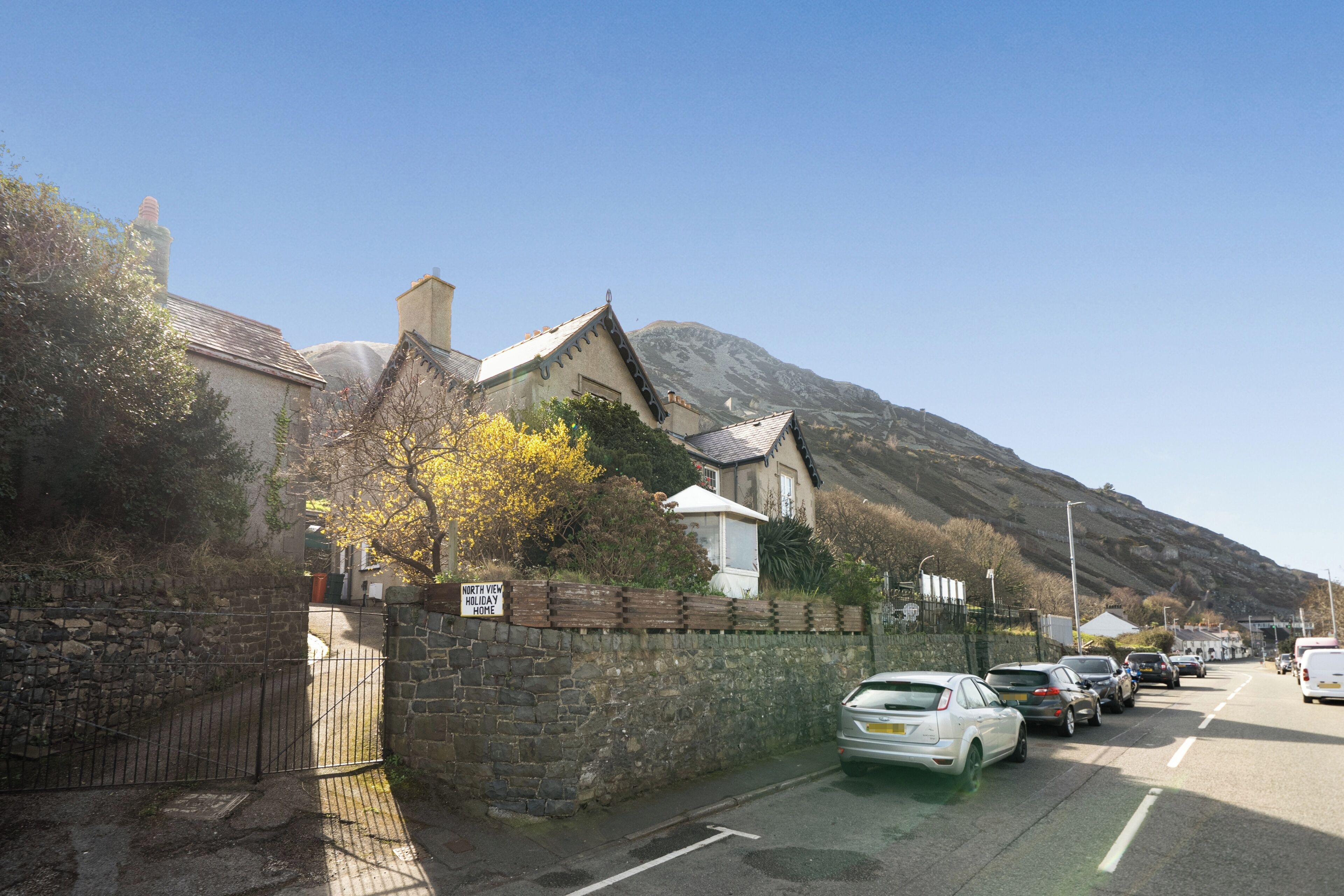 A street with parked cars, a stone wall, and a building with a sign.