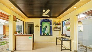 A reception area with a wooden reception desk, a ceiling fan, a wall-mounted shelf with bottles, and a large mural of a peacock. - Itsy Hotels Morjim Pride (Morjim)