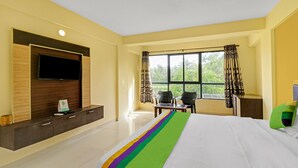 A hotel room with a bed, a TV mounted on a wooden panel, a desk with a chair, and a window with curtains. - Itsy Hotels Morjim Pride (Morjim)