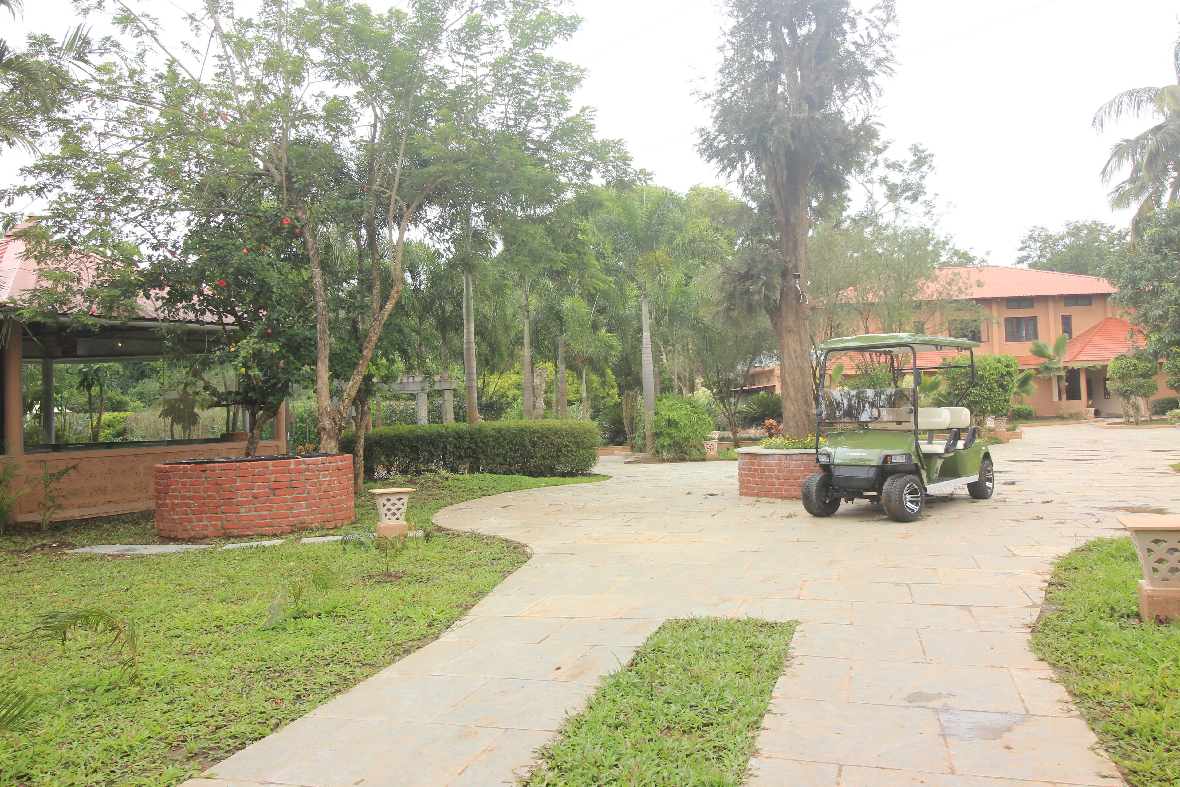 A paved pathway leading to a building with a red roof, surrounded by greenery and a golf cart parked nearby.