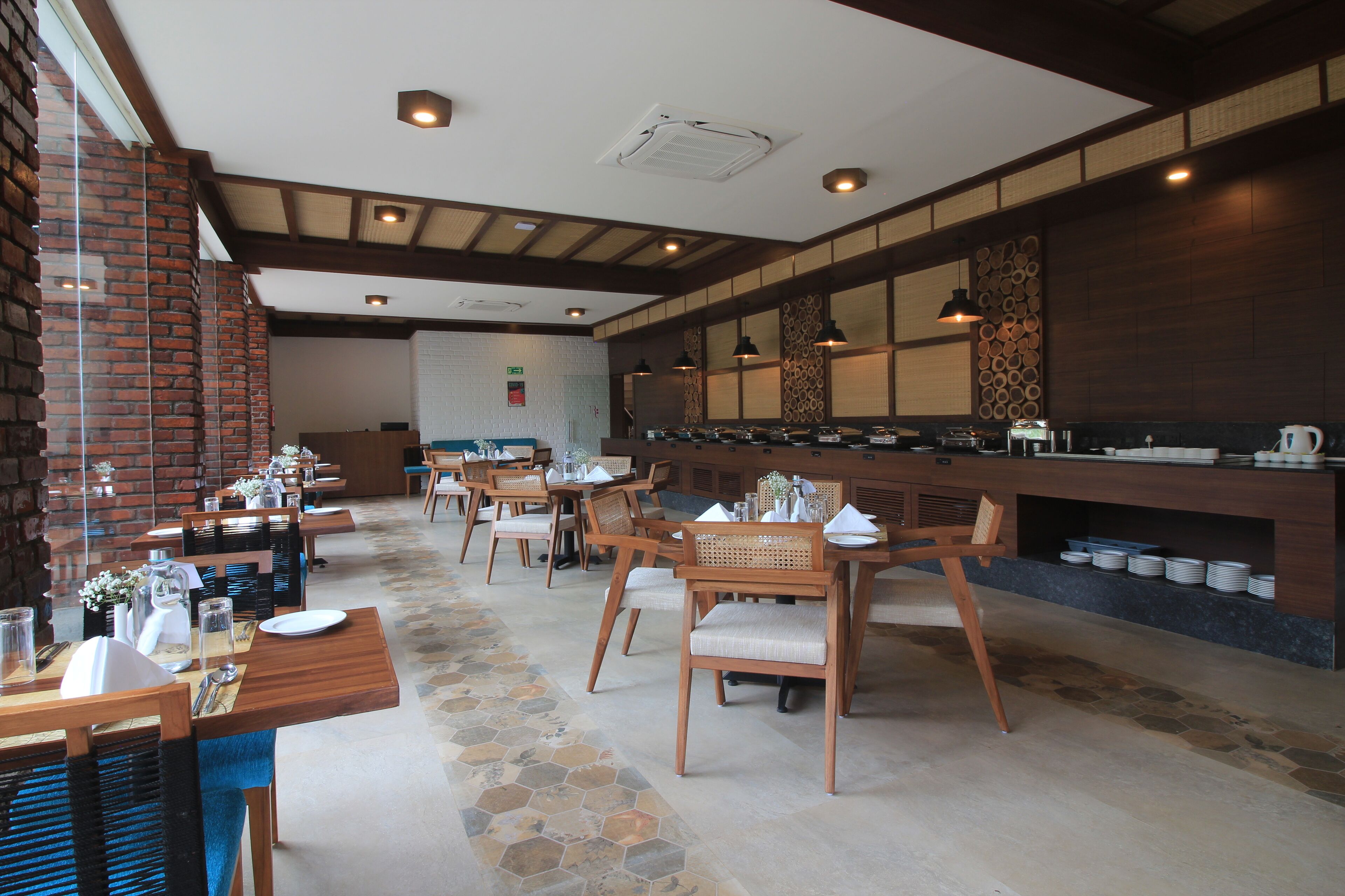 A restaurant with wooden tables and chairs, a brick wall, and a counter with dishes.