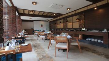 A restaurant with wooden tables and chairs, a brick wall, and a counter with dishes.