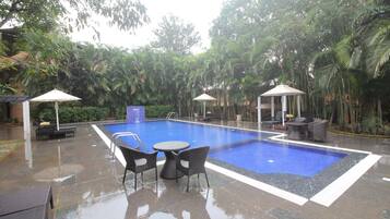 A swimming pool with lounge chairs and umbrellas, surrounded by palm trees and a tiled patio area.