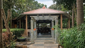 A covered entrance with stone pillars, a tiled pathway, and lush greenery. - Regenta Jungle Resort Kabini Springs (Heggadadevankote)
