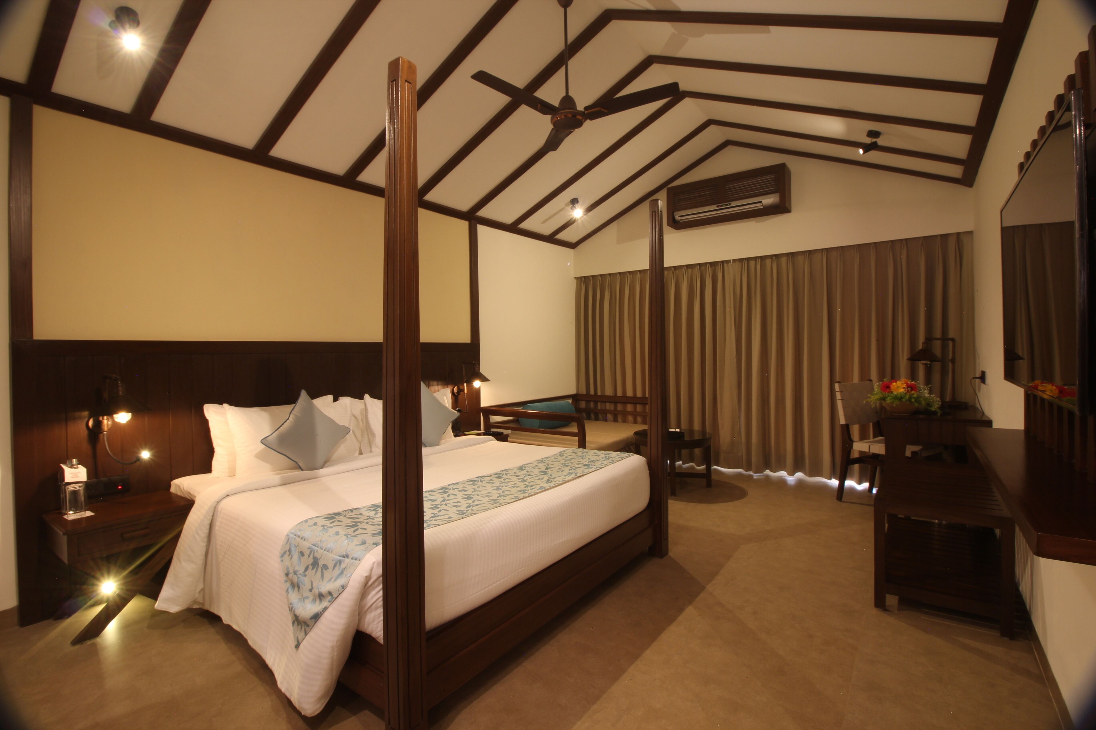 A spacious hotel room with a large bed, a desk, a chair, and a ceiling fan.