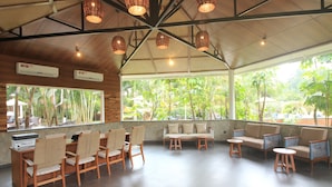 A spacious indoor area with wooden furniture, a large window with a view of greenery, and hanging wicker lights. - Regenta Jungle Resort Kabini Springs (Heggadadevankote)
