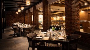 A restaurant with brick walls, glass tables, and wicker chairs. - Regenta Jungle Resort Kabini Springs (Heggadadevankote)
