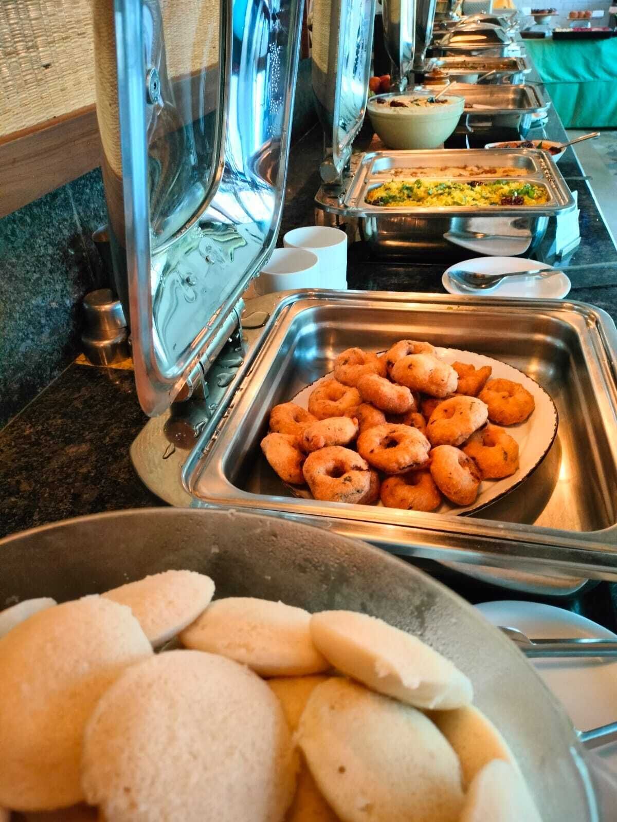 Un bufé con diversos alimentos, incluyendo una bandeja de buñuelos dorados y un bol de panecillos blancos.