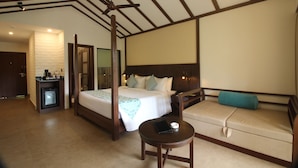 A hotel room with a large bed, a sofa, a small table, and a minibar. - Regenta Jungle Resort Kabini Springs (Heggadadevankote)
