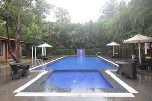 A rectangular swimming pool with a blue interior, surrounded by lounge chairs and umbrellas. - Regenta Jungle Resort Kabini Springs (Heggadadevankote)